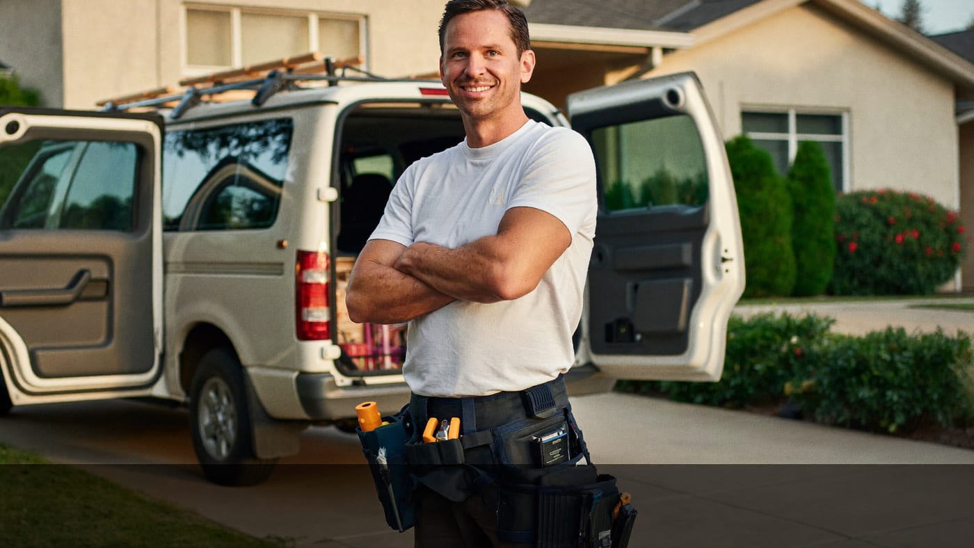 A local home services contractor standing beside his work van in a suburban driveway